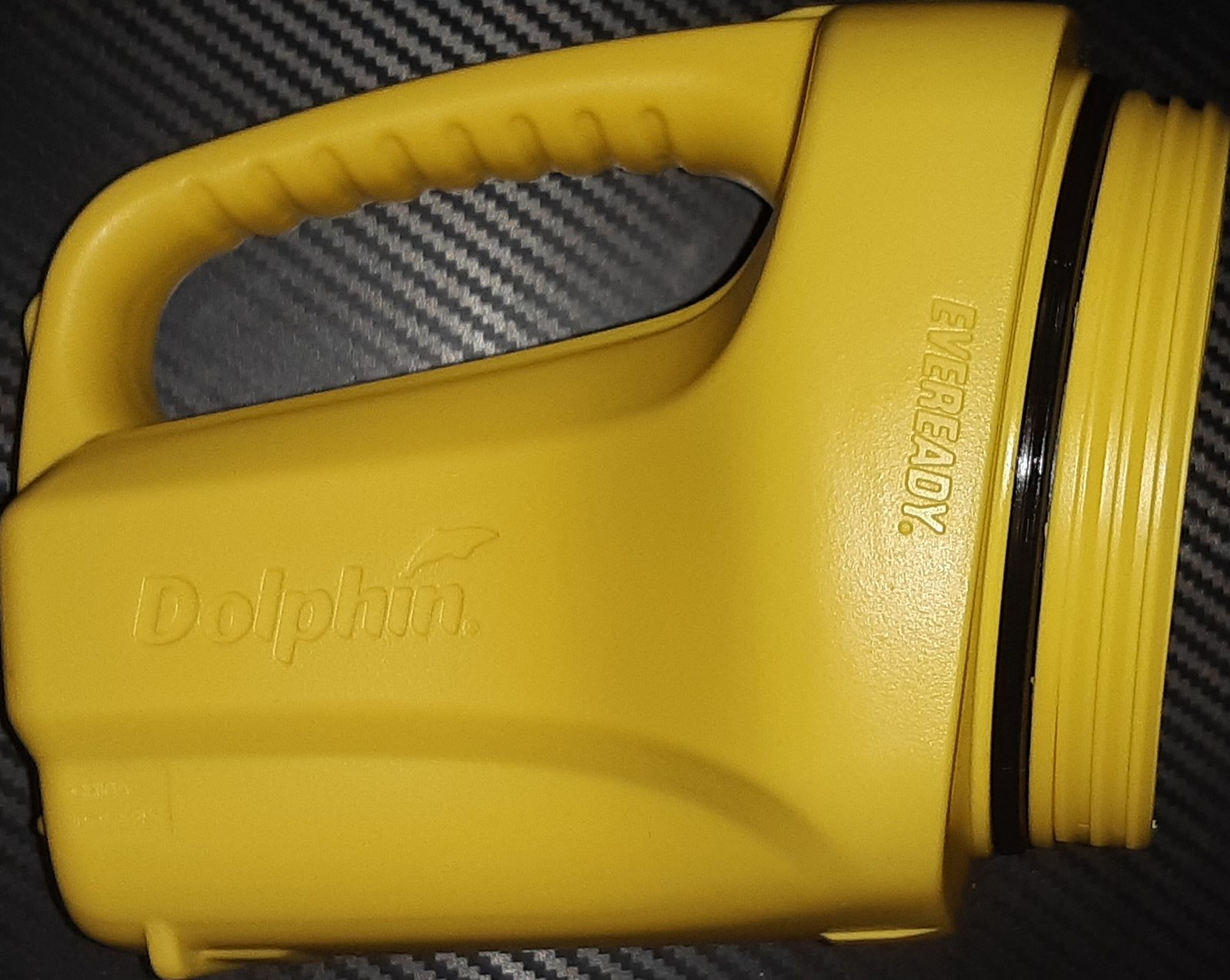 Side view photograph of a yellow Dolphin torch on a carbon-fibre patterned surface