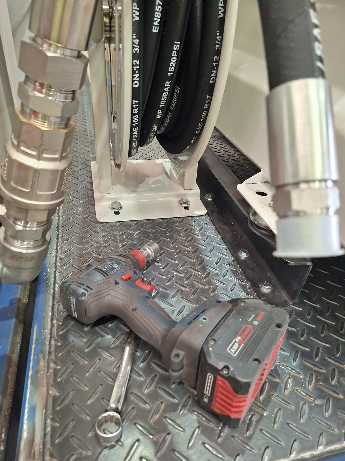 Hydraulic hose and fittings from the hose reel on unpainted checker plate during a test fit, an impact driver beside it