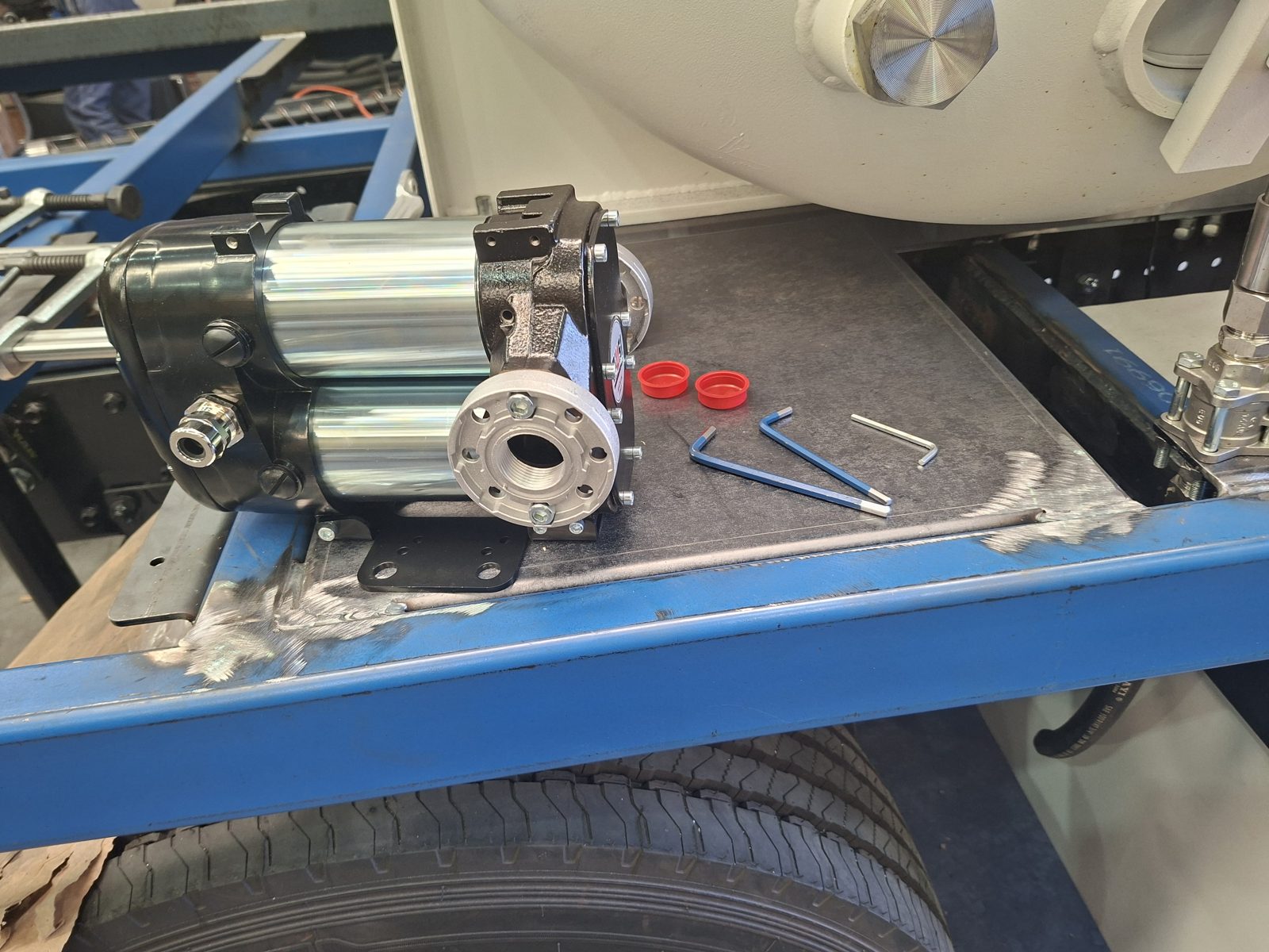 A pump bolted to a blue chassis rail with tools beside it